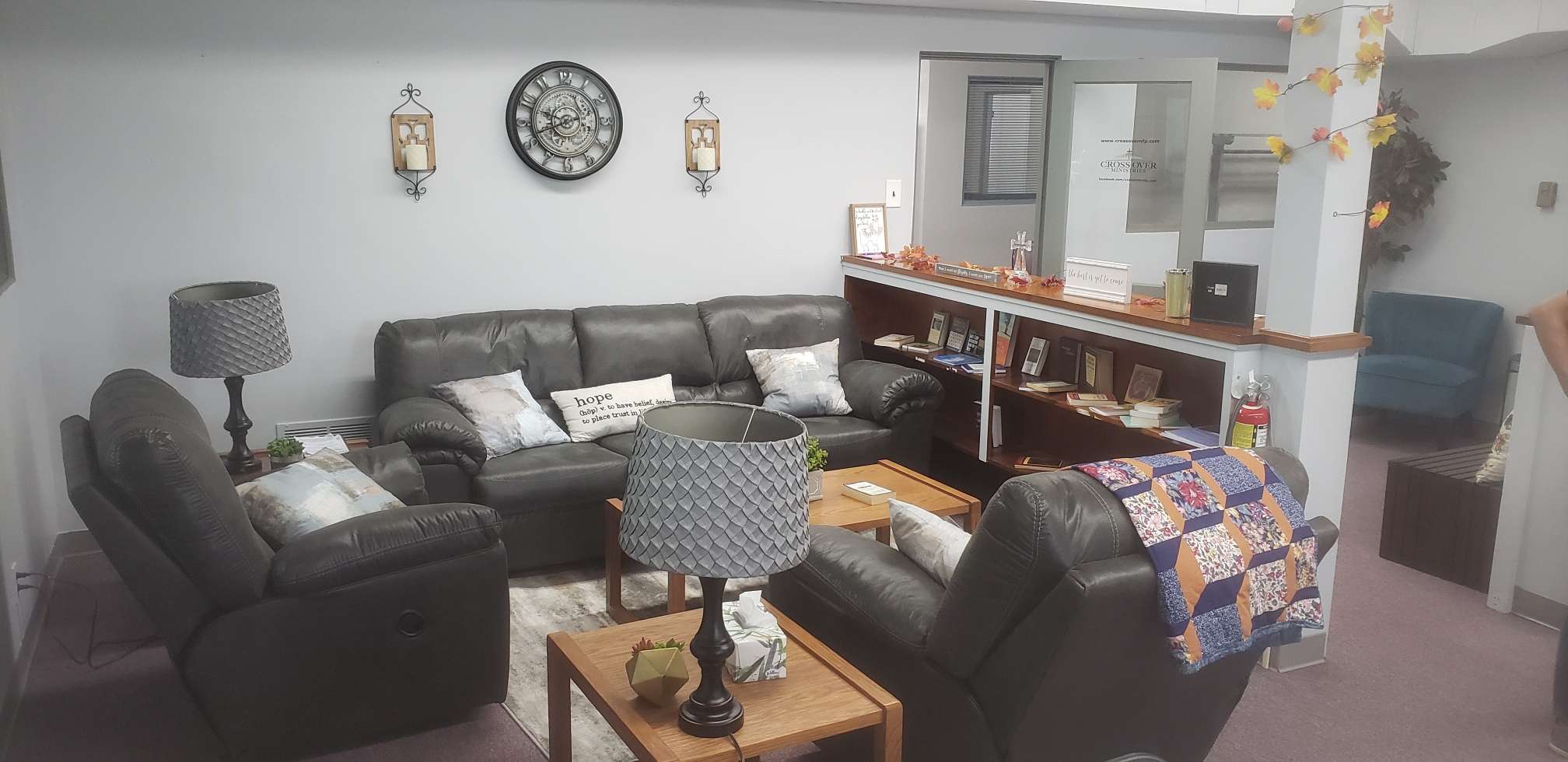 dark leather chairs and sofa, brown wooden end tables and book shelf, silver and white pillows and lamps in a safe comfortable area