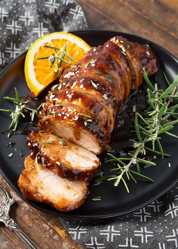 sliced tender pork loin meat with orange slice and green garnish on black serving platter
