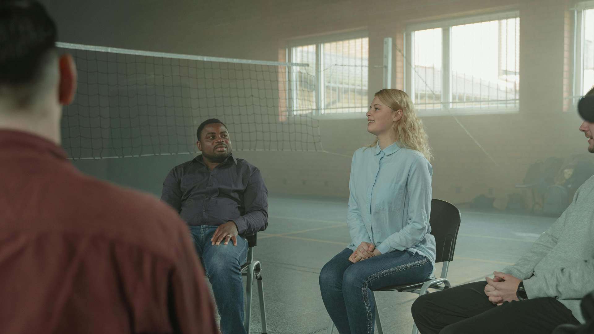 dark skinned man listens attentively to young blond woman sharing in a circle meeting