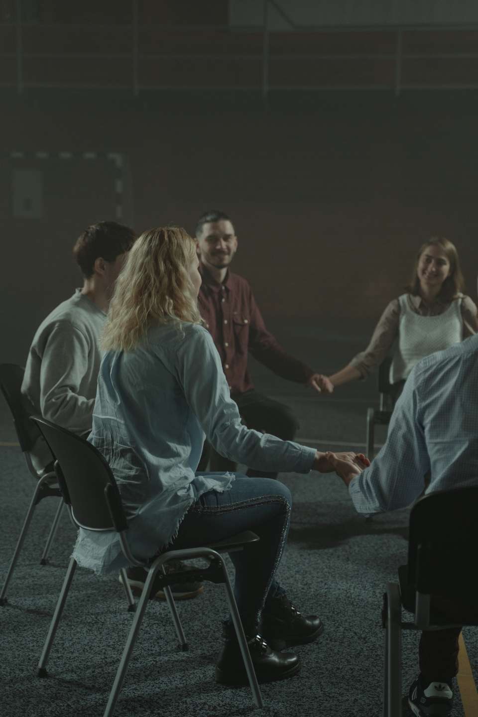 male and female persons sit in circle holding hands with careful smiles