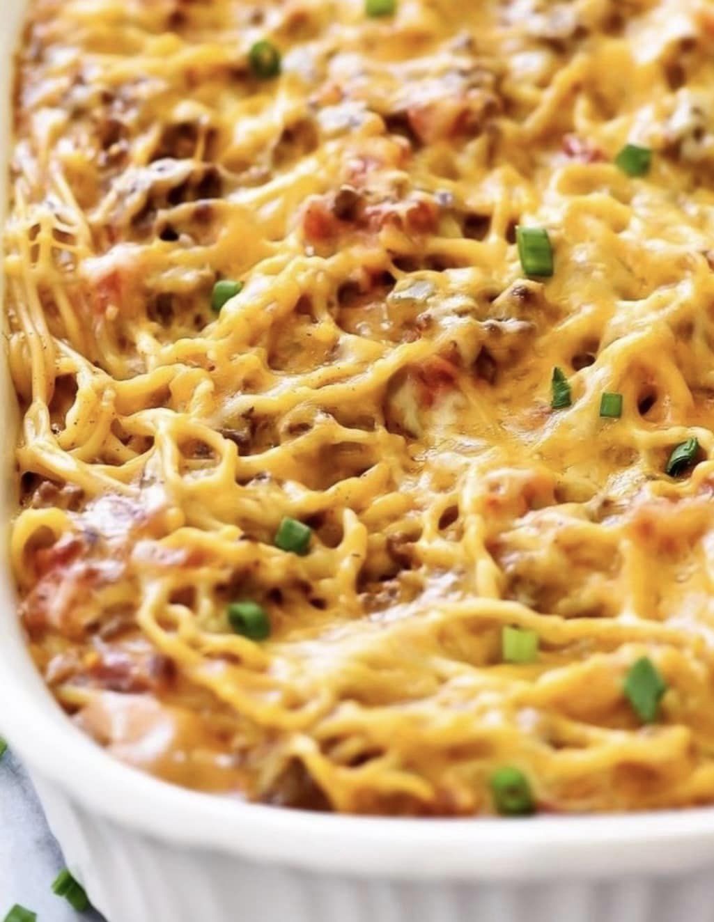orange cheese and sauce on baked spaghetti noodles in casserole dish