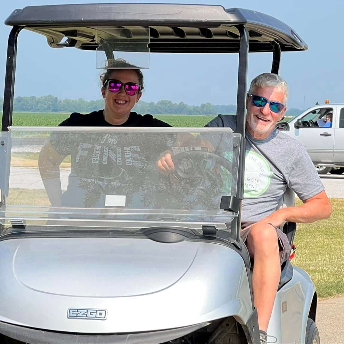 woman and man wearing sunglasses driving golf cart outdoors