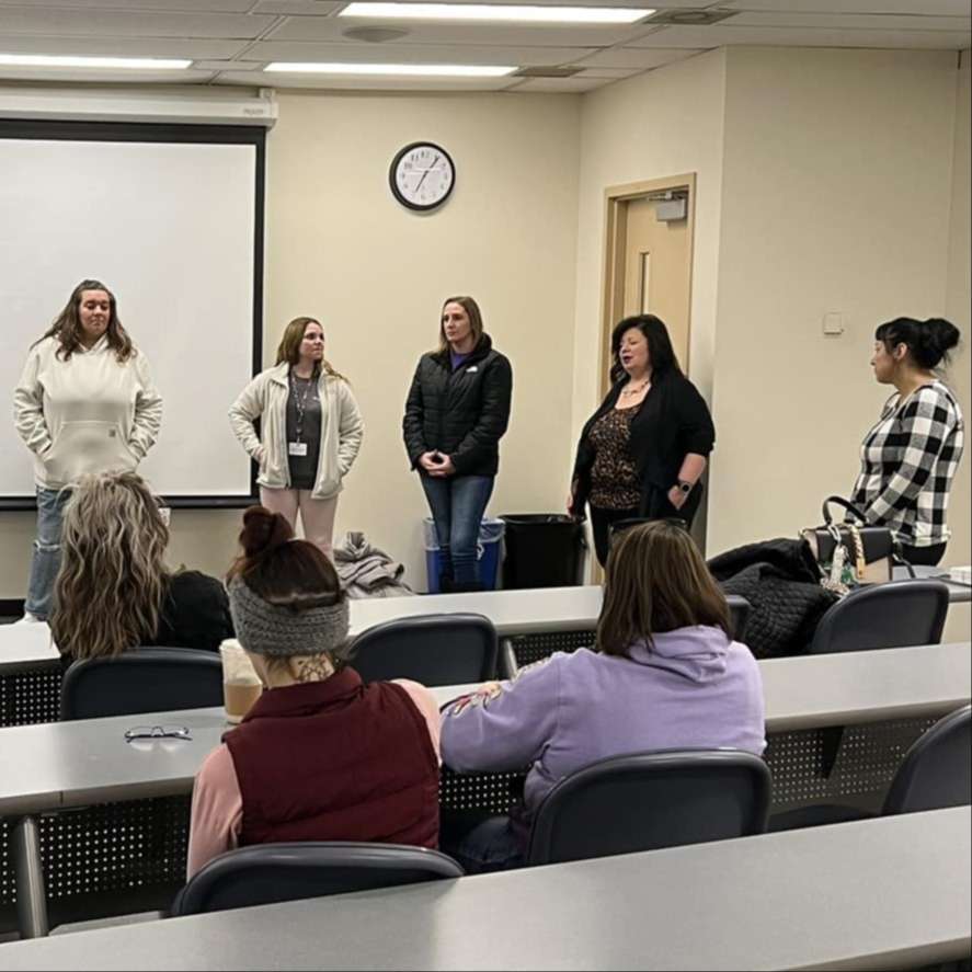 five women stand in front of a college lecture classroom
