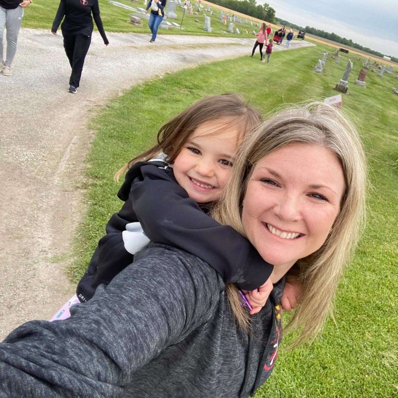 blond woman and small child take a selfie in cemetery with green grass and stone path