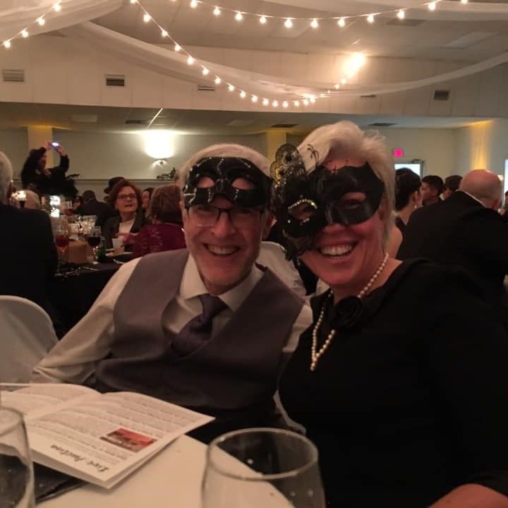 man and woman smile in black and silver masks at hospital fundraising dinner